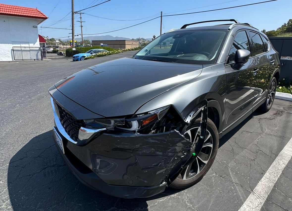 A gray car with a damaged bumper is parked in a parking lot.