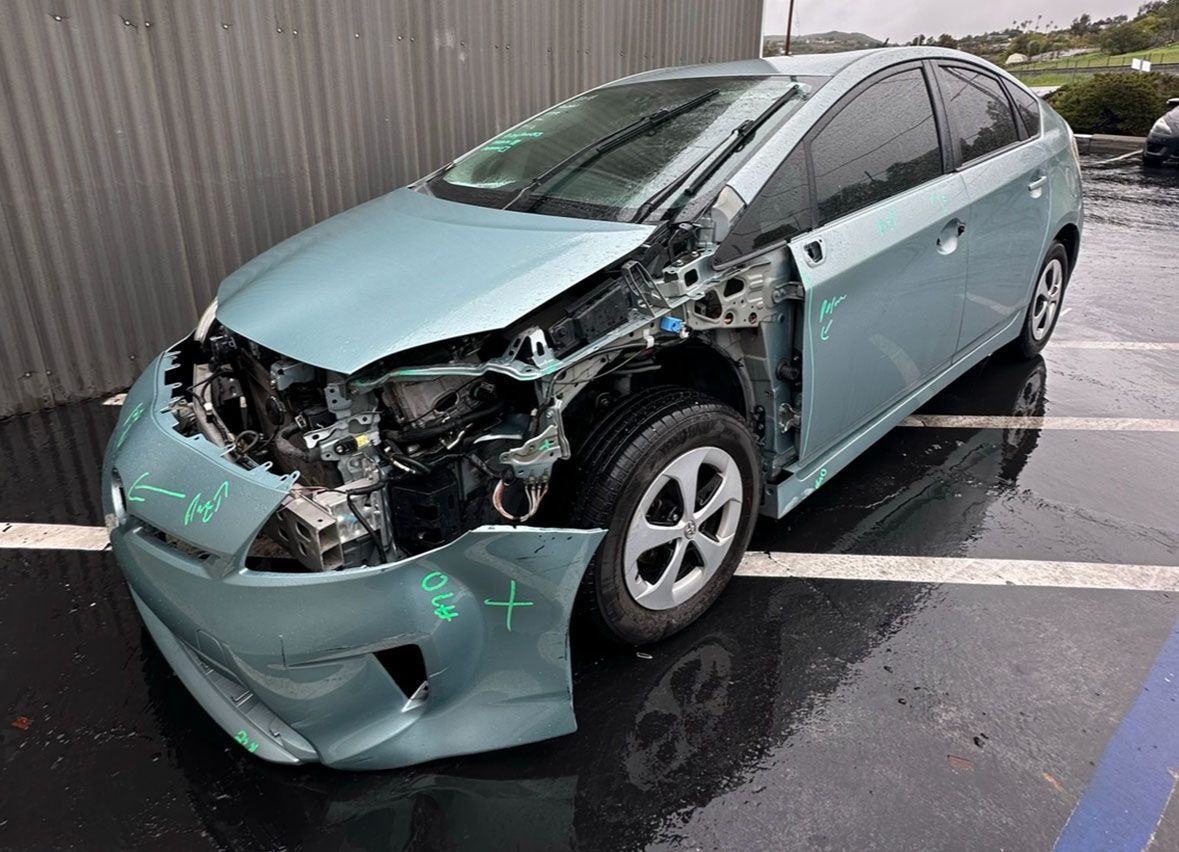 A damaged toyota prius is parked in a parking lot.