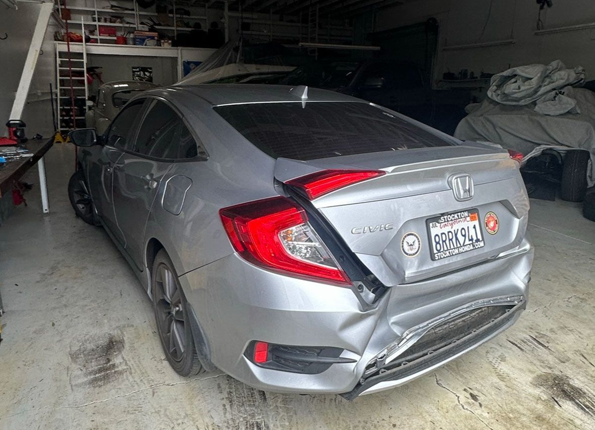 A damaged honda civic is parked in a garage.