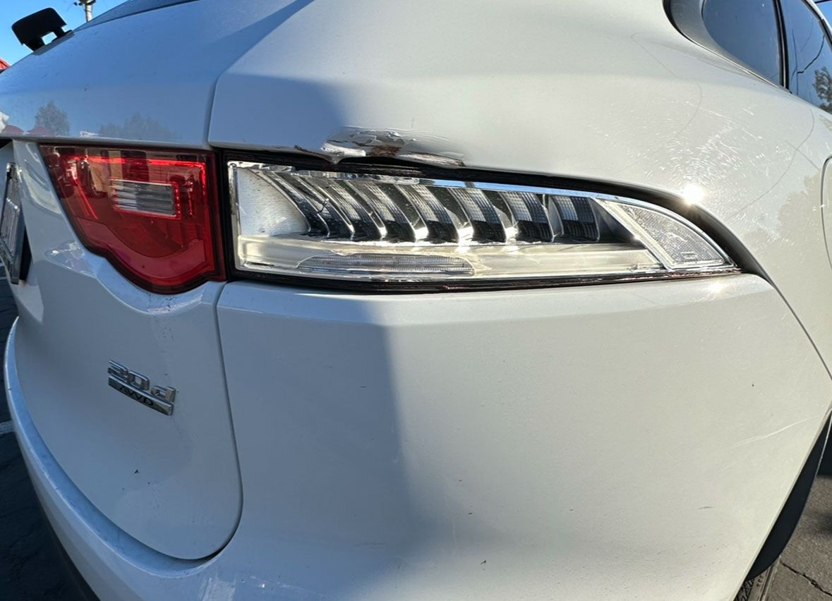 A white car with a damaged bumper is parked in a parking lot.