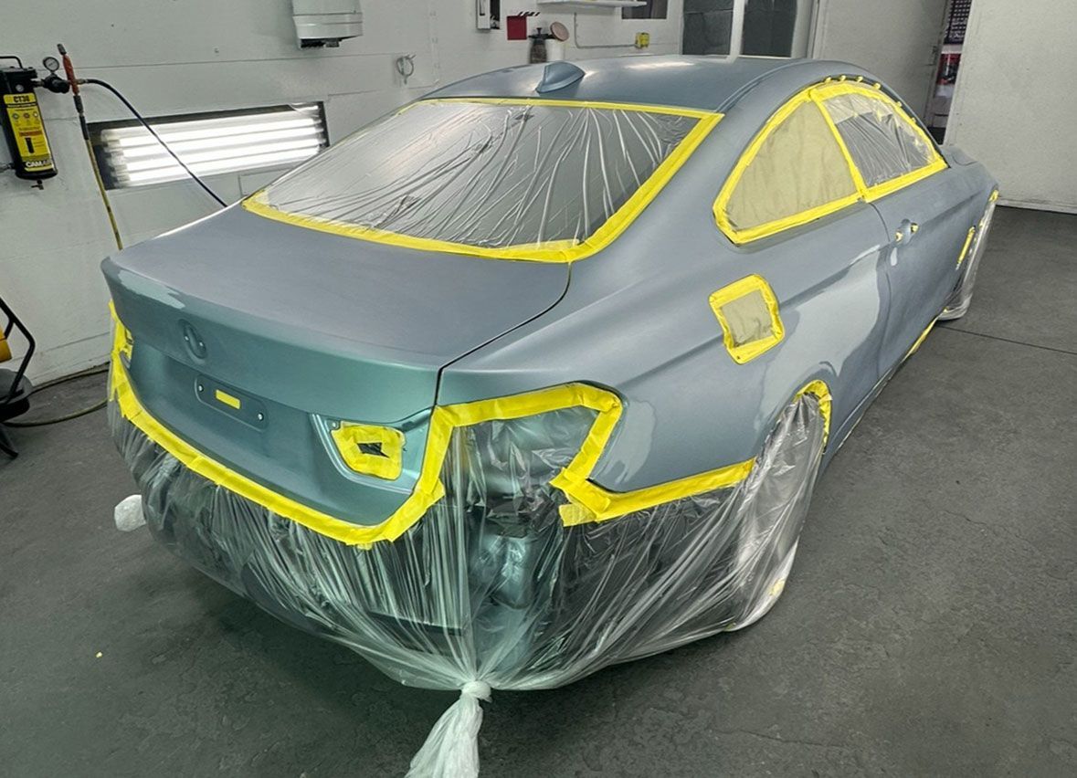 A car is wrapped in plastic while being painted in a garage.