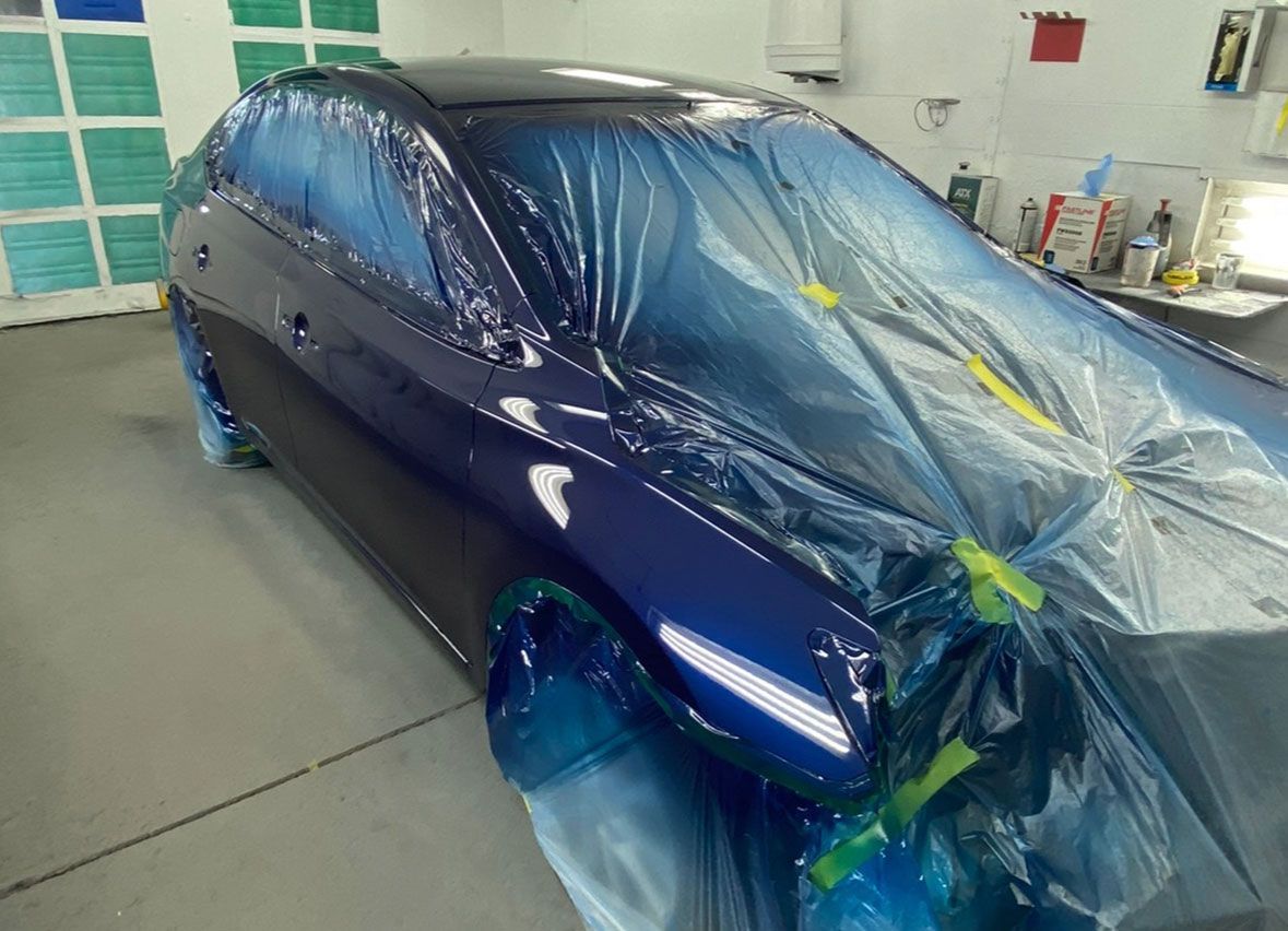 A blue car is wrapped in plastic and ready to be painted