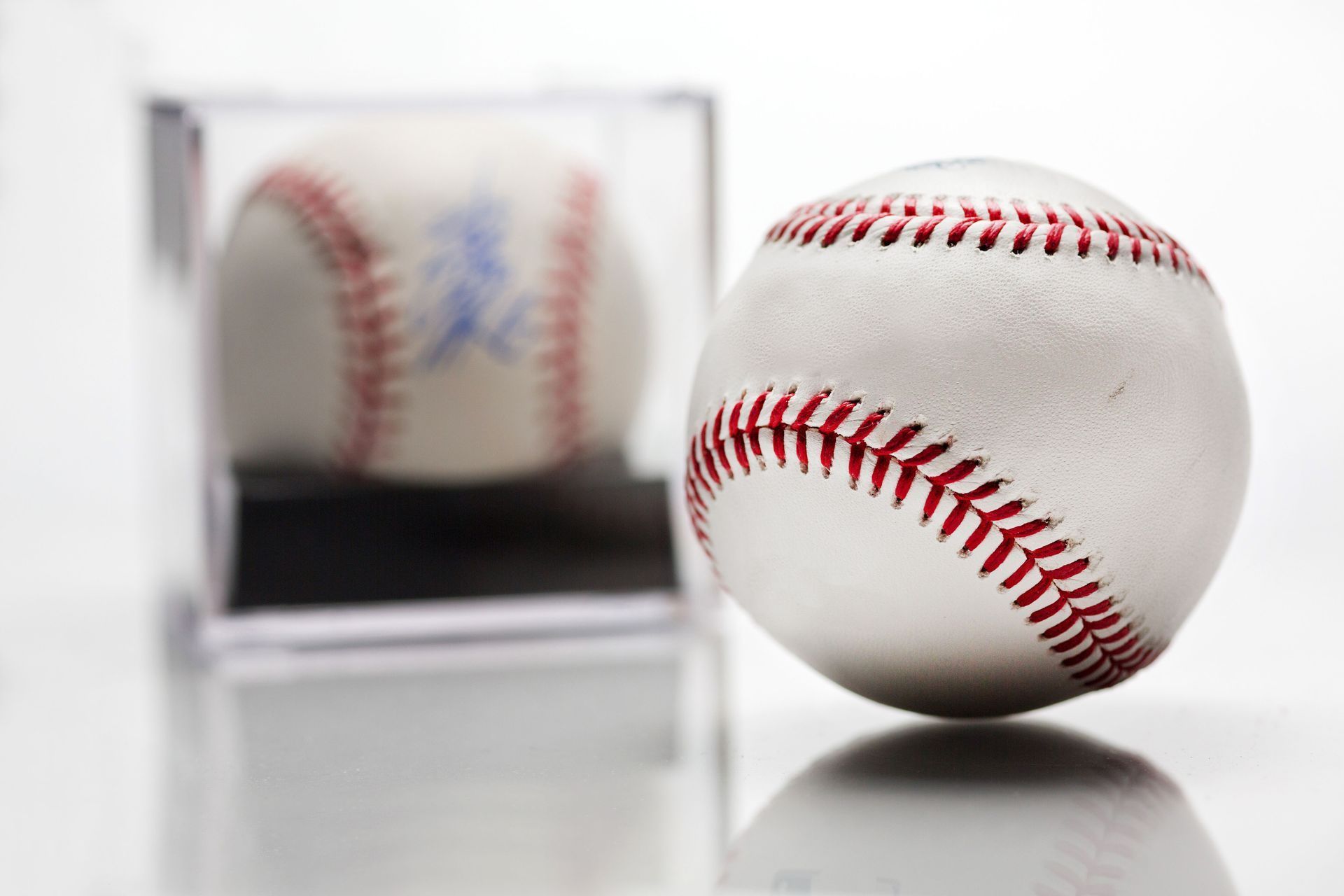 A white baseball with red stitching in front of a mirrored reflection on a glossy surface