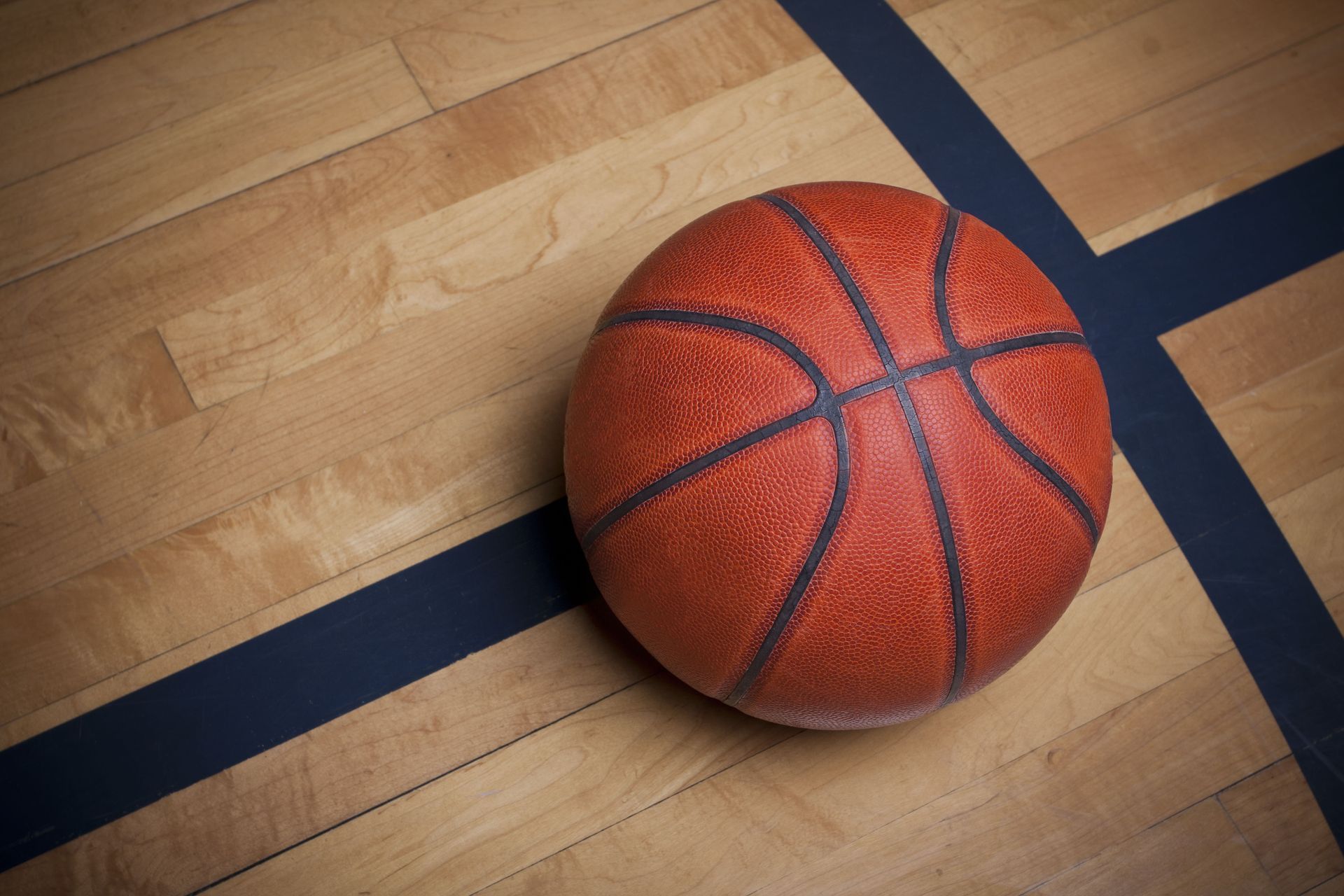 Orange basketball on a wooden gym floor with blue court lines.