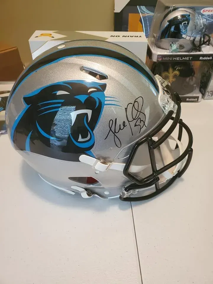 Carolina Panthers silver football helmet with black face mask and signed logo, on a table.