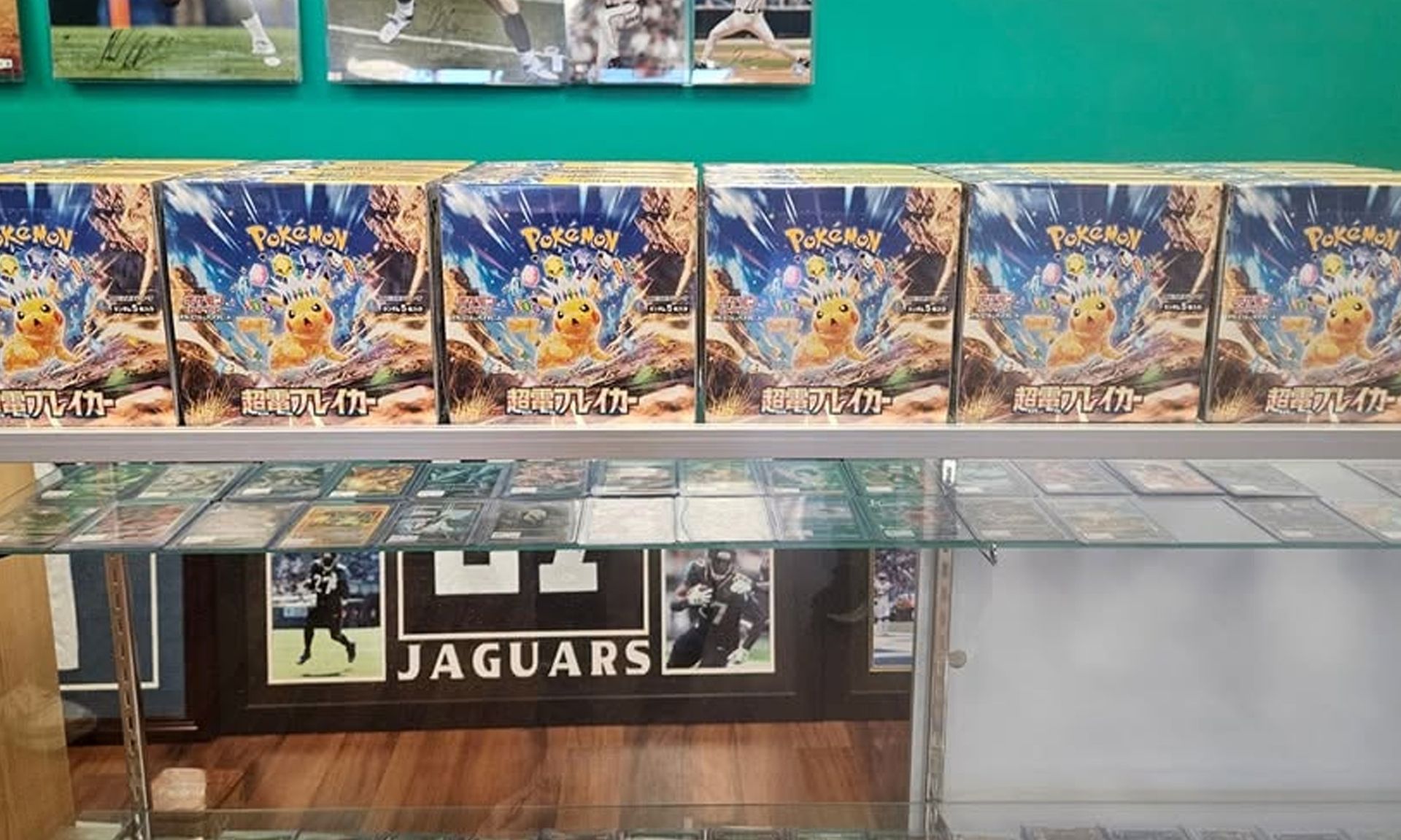 Table display with stacked Pokémon card boxes and booster packs above a Jaguars sign in a store