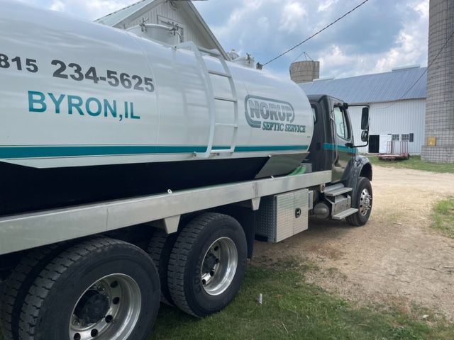 A Byron, IL tanker truck is parked in front of a barn.