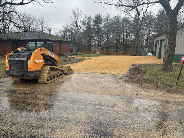 A bulldozer is driving down a dirt road next to a house.
