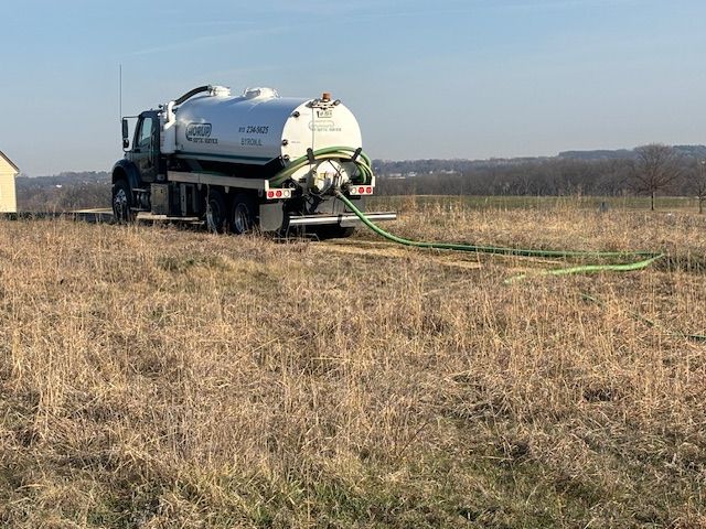 A vacuum truck is driving through a dry grass field.