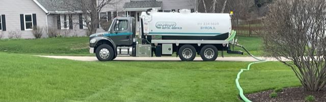 A septic tank truck is driving down a driveway next to a house.