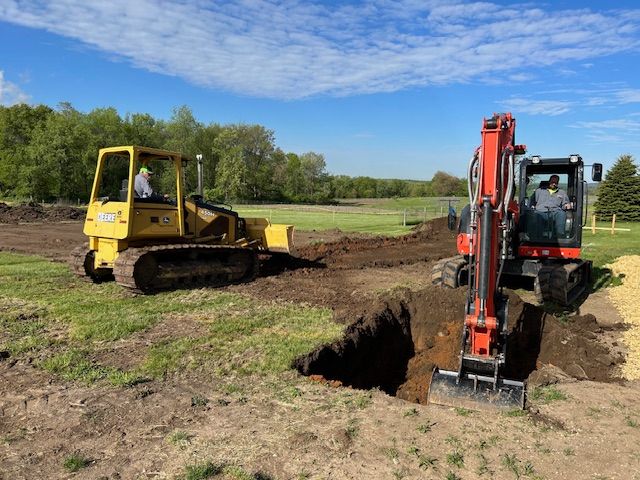 A bulldozer and an excavator are digging a hole in a field.
