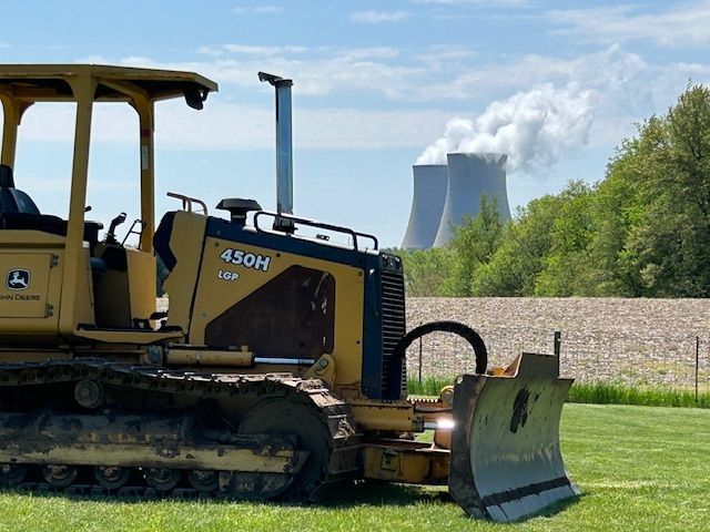 A bulldozer is parked in a field with a nuclear power plant in the background.