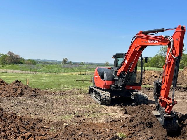 A red excavator is digging a hole in the dirt in a field.
