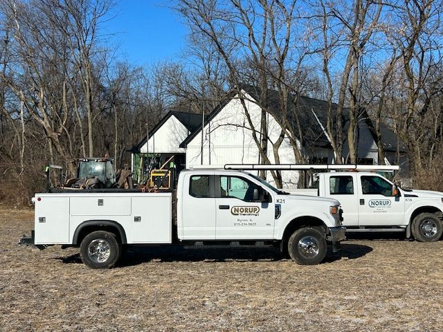 Two white trucks are parked in a field in front of a house.