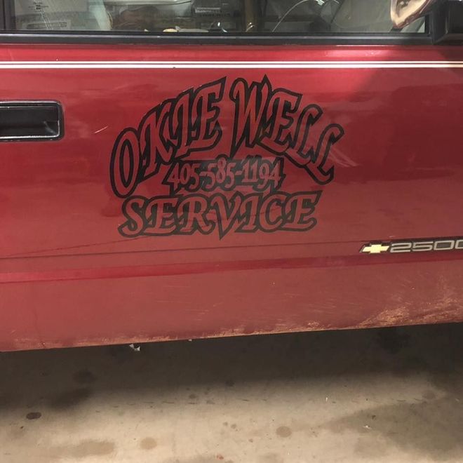 Red truck door with black "Okie Well Service" logo and phone number; rusty lower panel.
