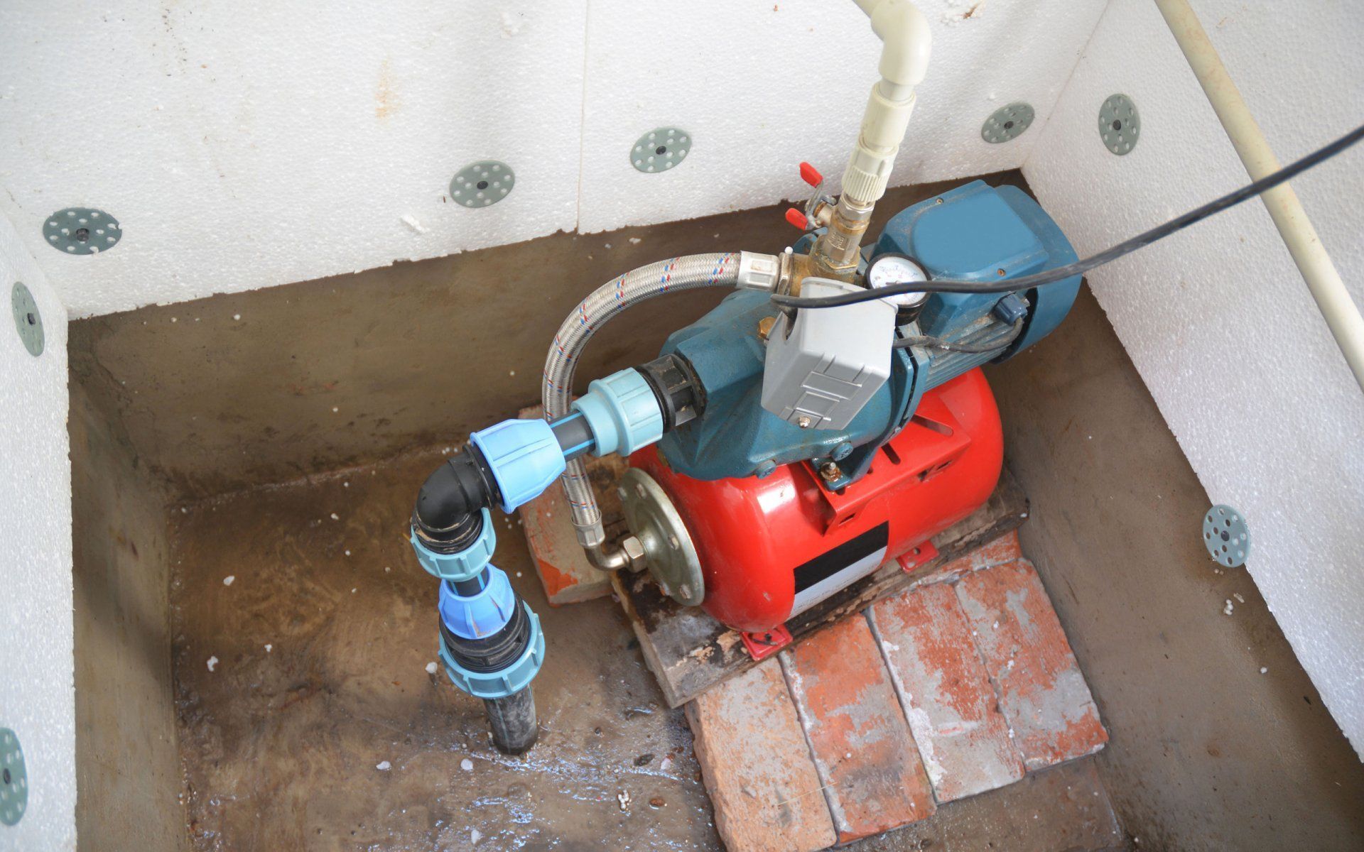 Water pump inside a small enclosure, red and teal colored, connected to pipes.