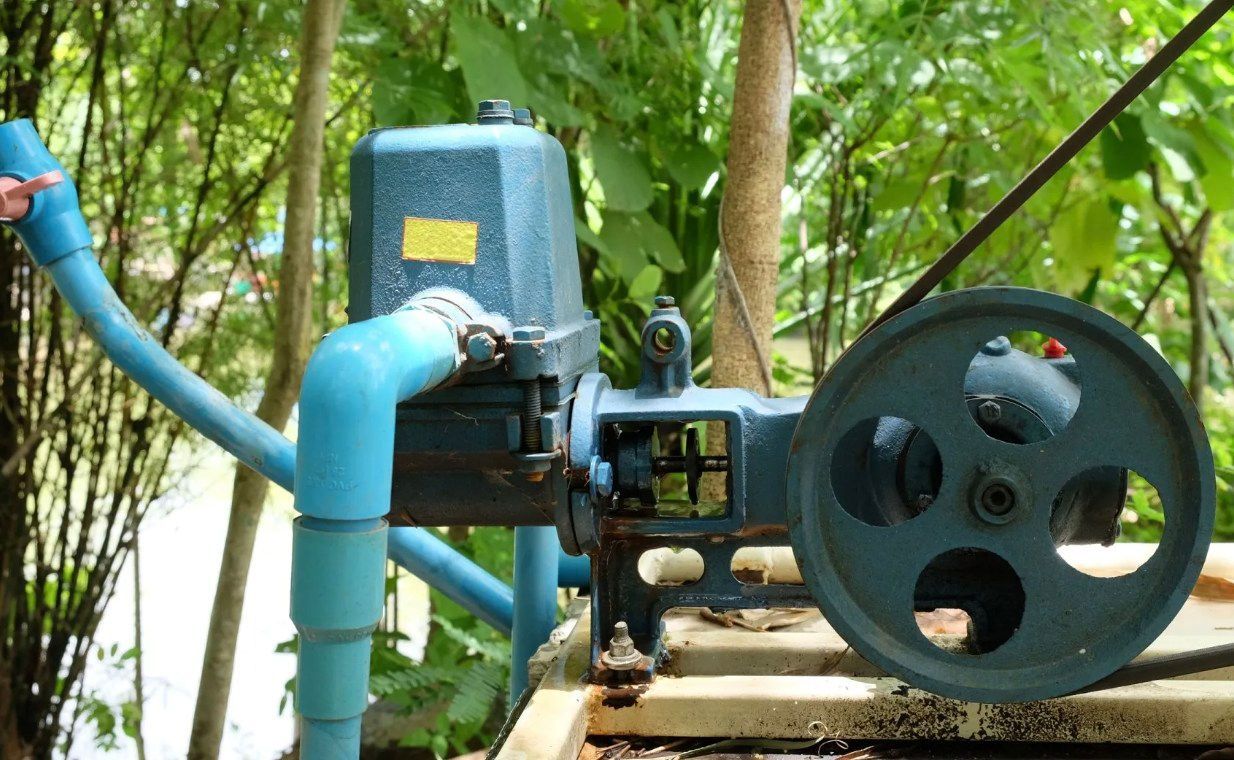 Blue water pump system with large pulley in outdoor setting.