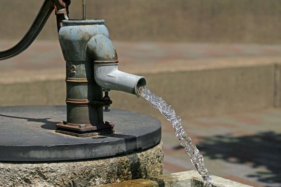 Water flows from an old, blue water pump with a black handle. Stone base, background.