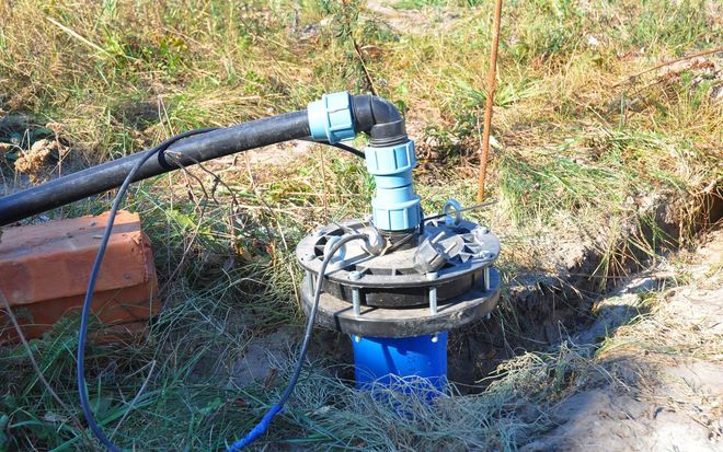 Well pump with blue piping and black hose in a grassy area.