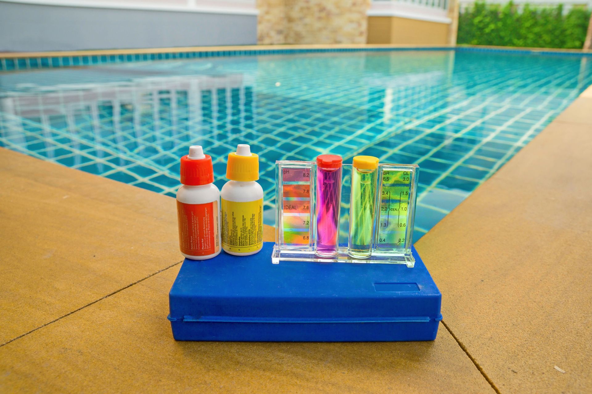 Pool water testing kit with chemical bottles and color-coded comparison vials, beside a turquoise pool.