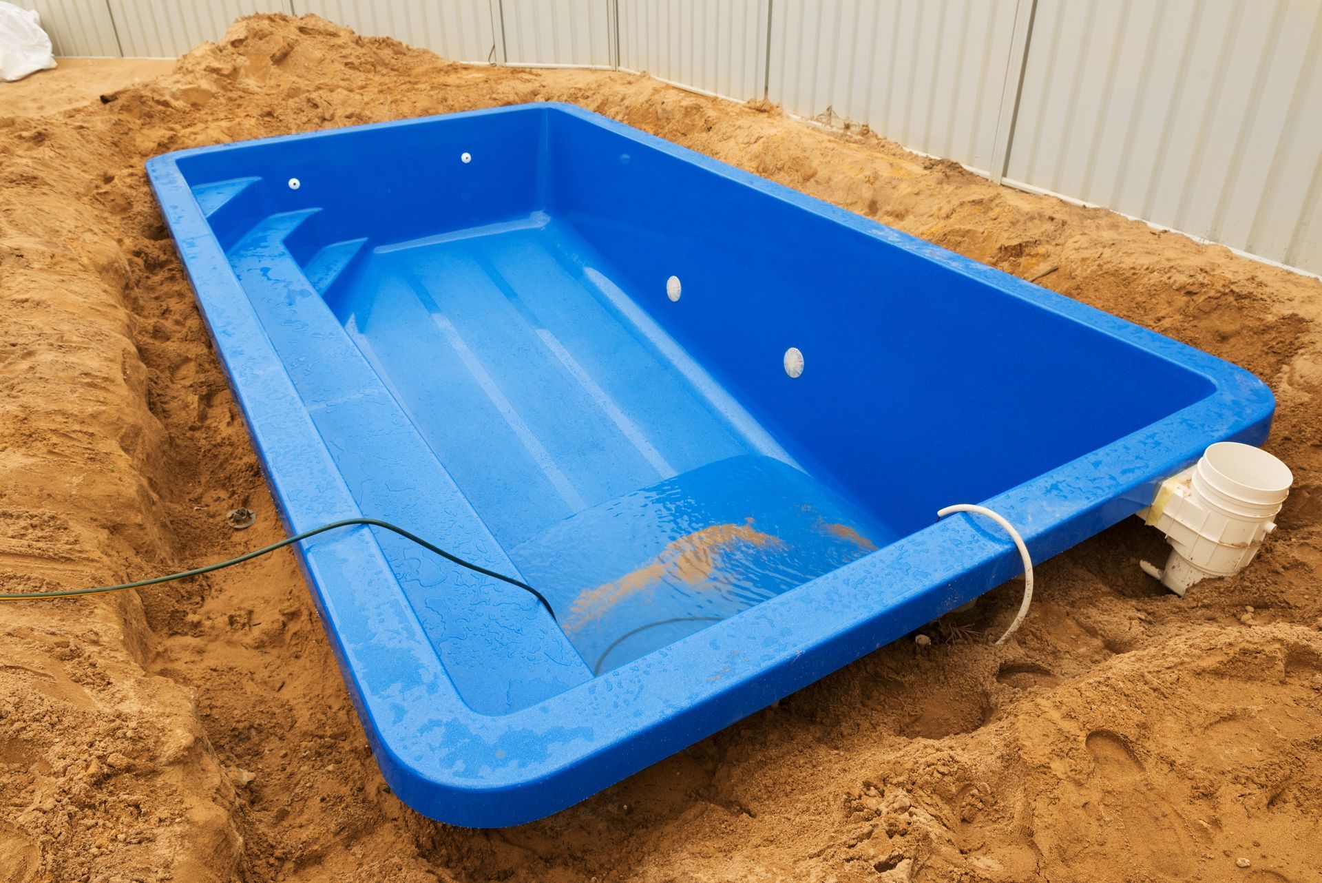 Blue rectangular in-ground pool shell in a sandy excavation site.