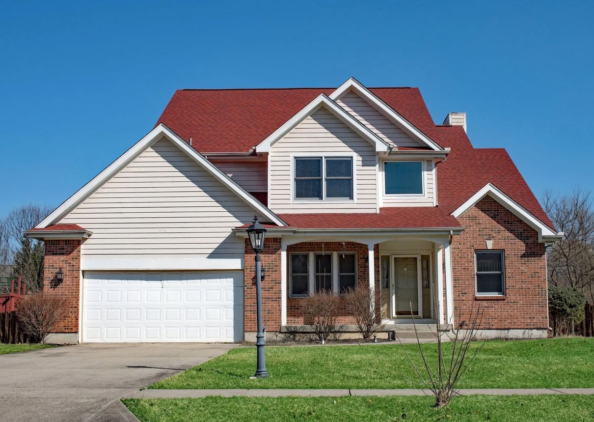 Two-story house with red roof, white siding, brick accents, and a two-car garage under a blue sky.