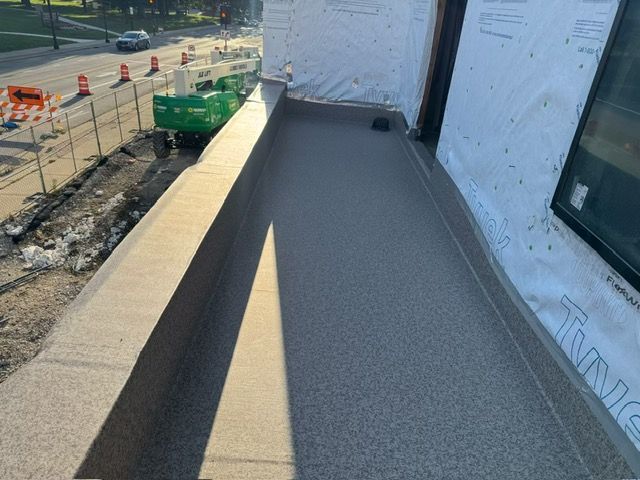 A newly installed grey textured balcony floor next to a building wall with white house wrap, overlooking a street.