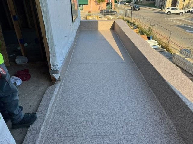 A newly coated gray speckled balcony deck under construction, extending from an unfinished building interior.
