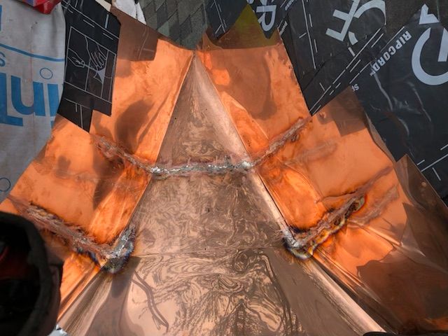 Copper roof flashing installed on a valley intersection, showing soldered seams against black underlayment.