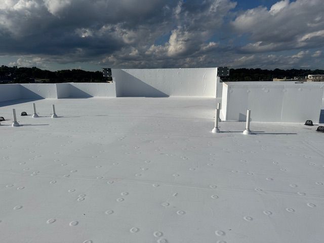 A bright white, flat rooftop with several vertical vent pipes under a cloudy blue sky.