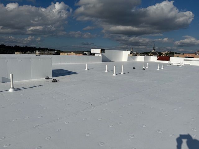 Flat white roof surface with several vertical vent pipes against a blue sky with white clouds.