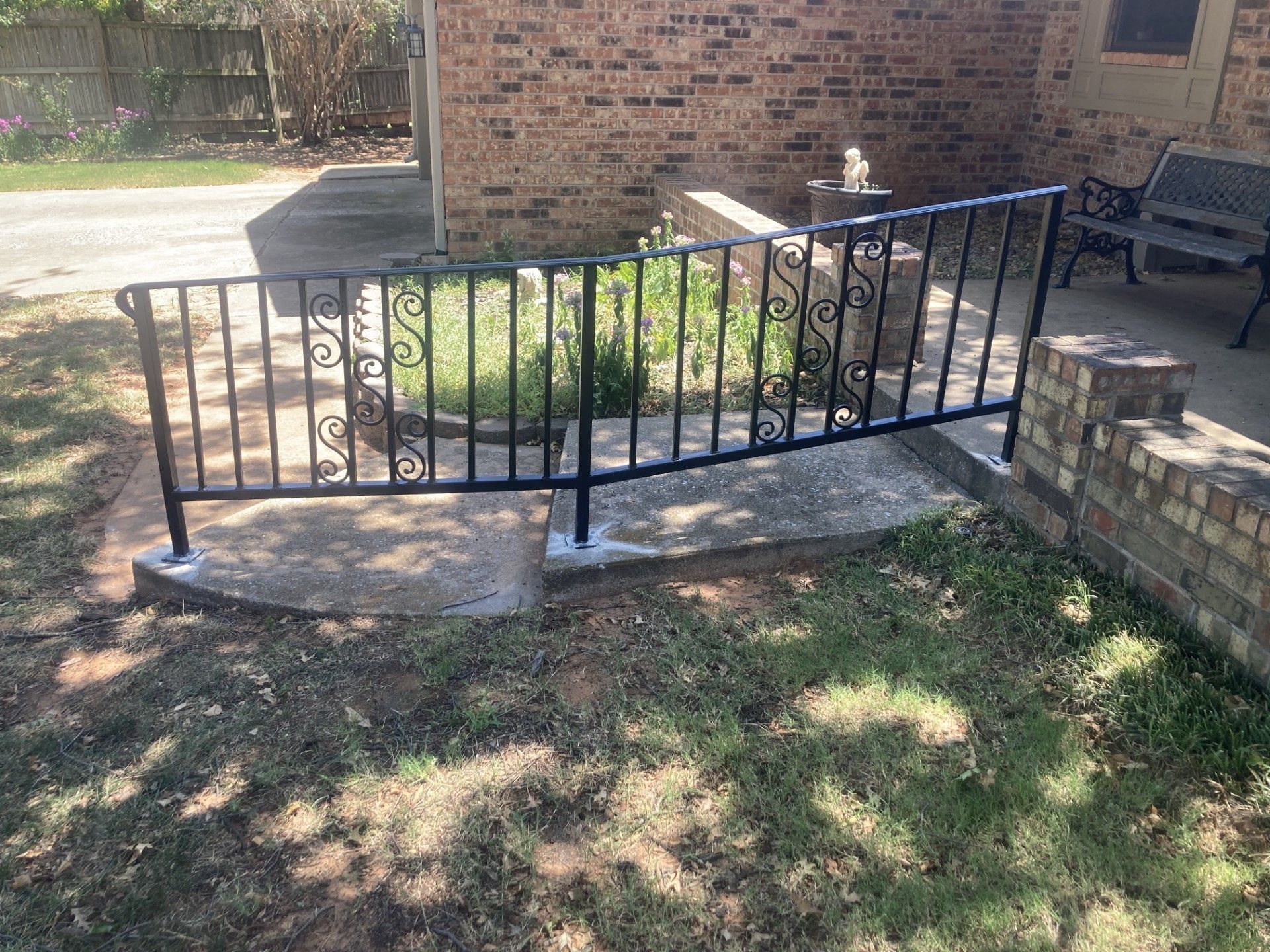Black metal railing beside a brick building, bordering a curved concrete ramp in a sunny yard.