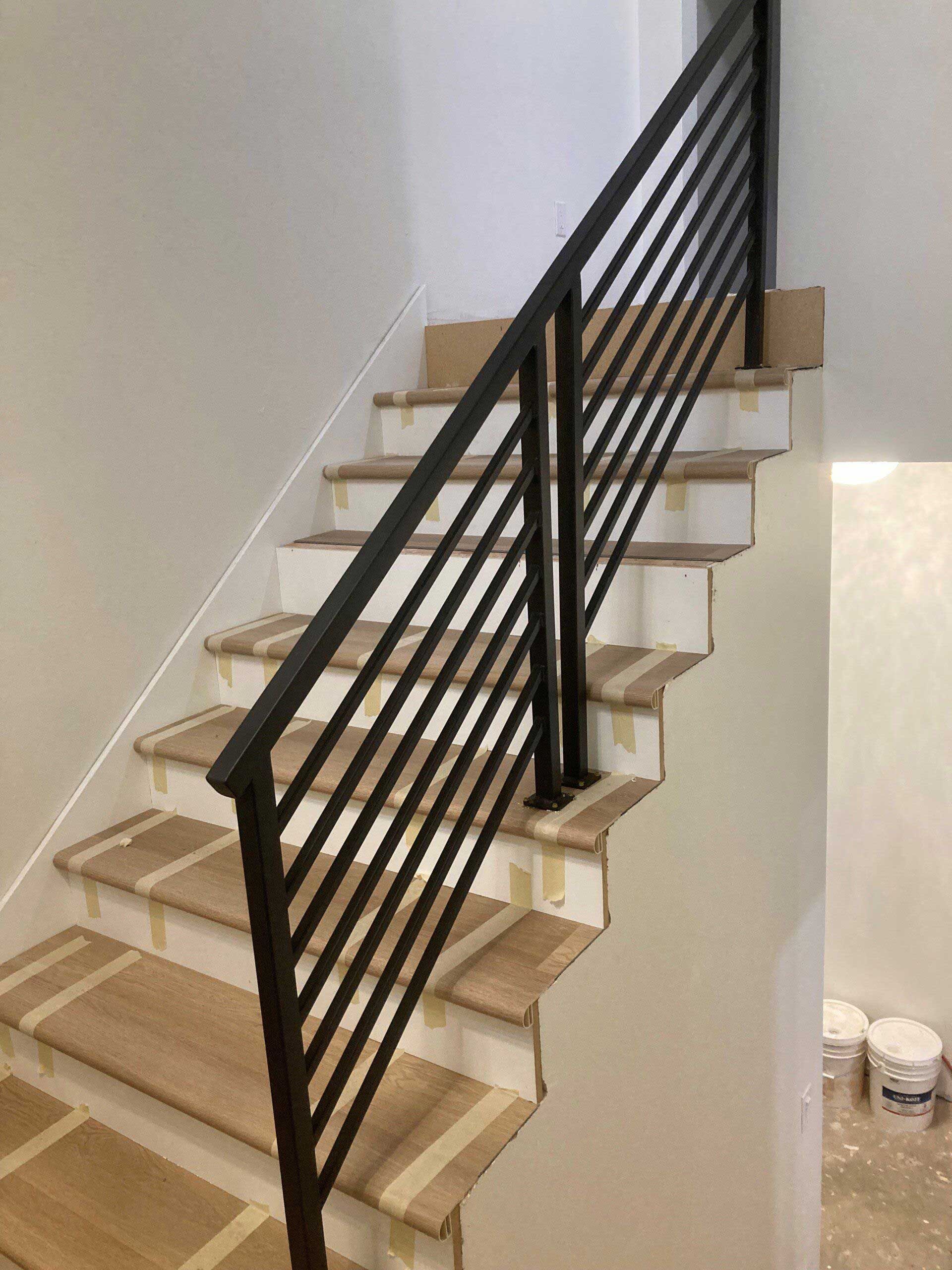 Staircase with black metal railing. Light wooden steps. White walls.
