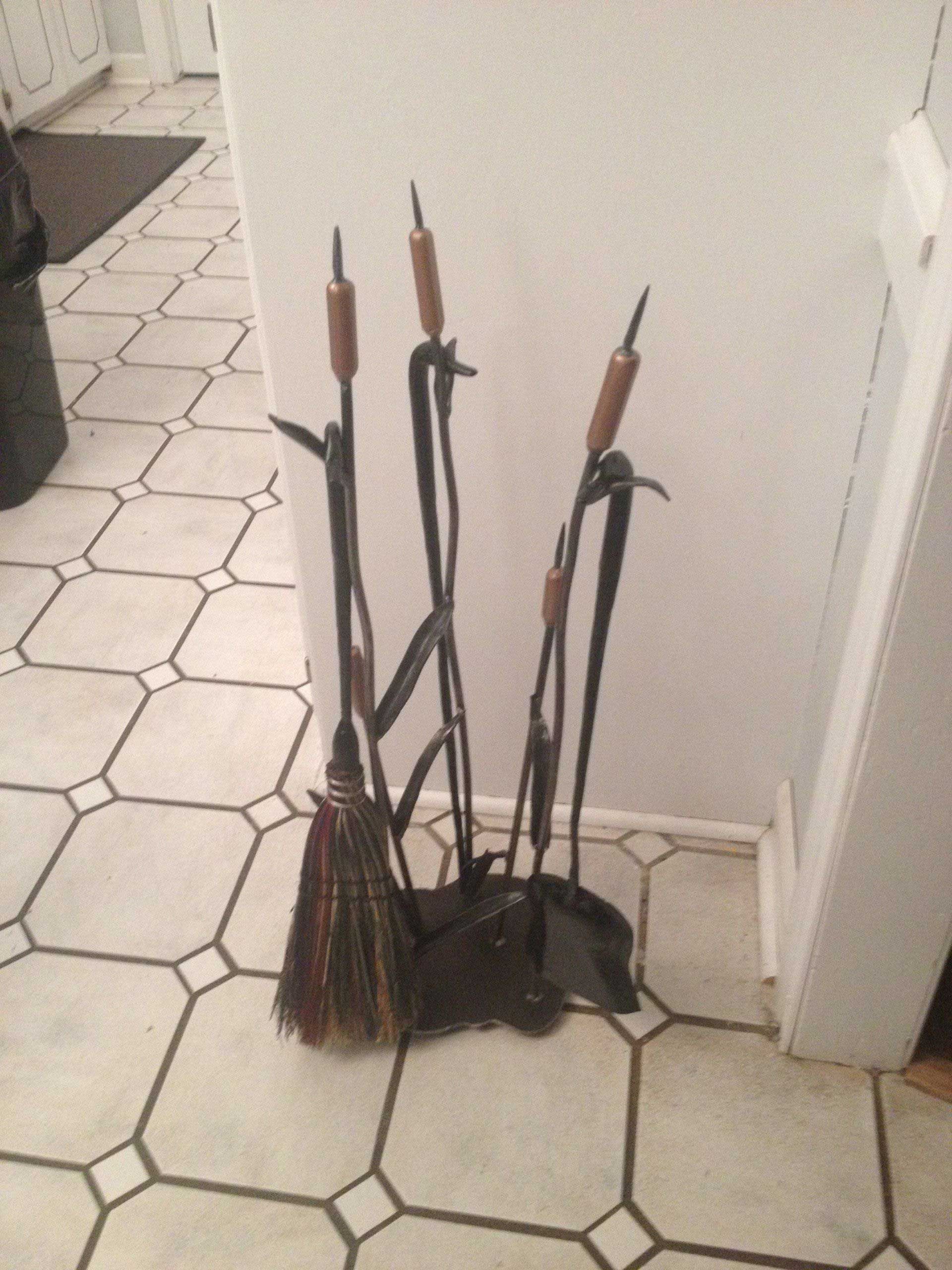 Fireplace tools stand: black metal stand with tools including a brush, poker, and shovel, on a tiled floor.