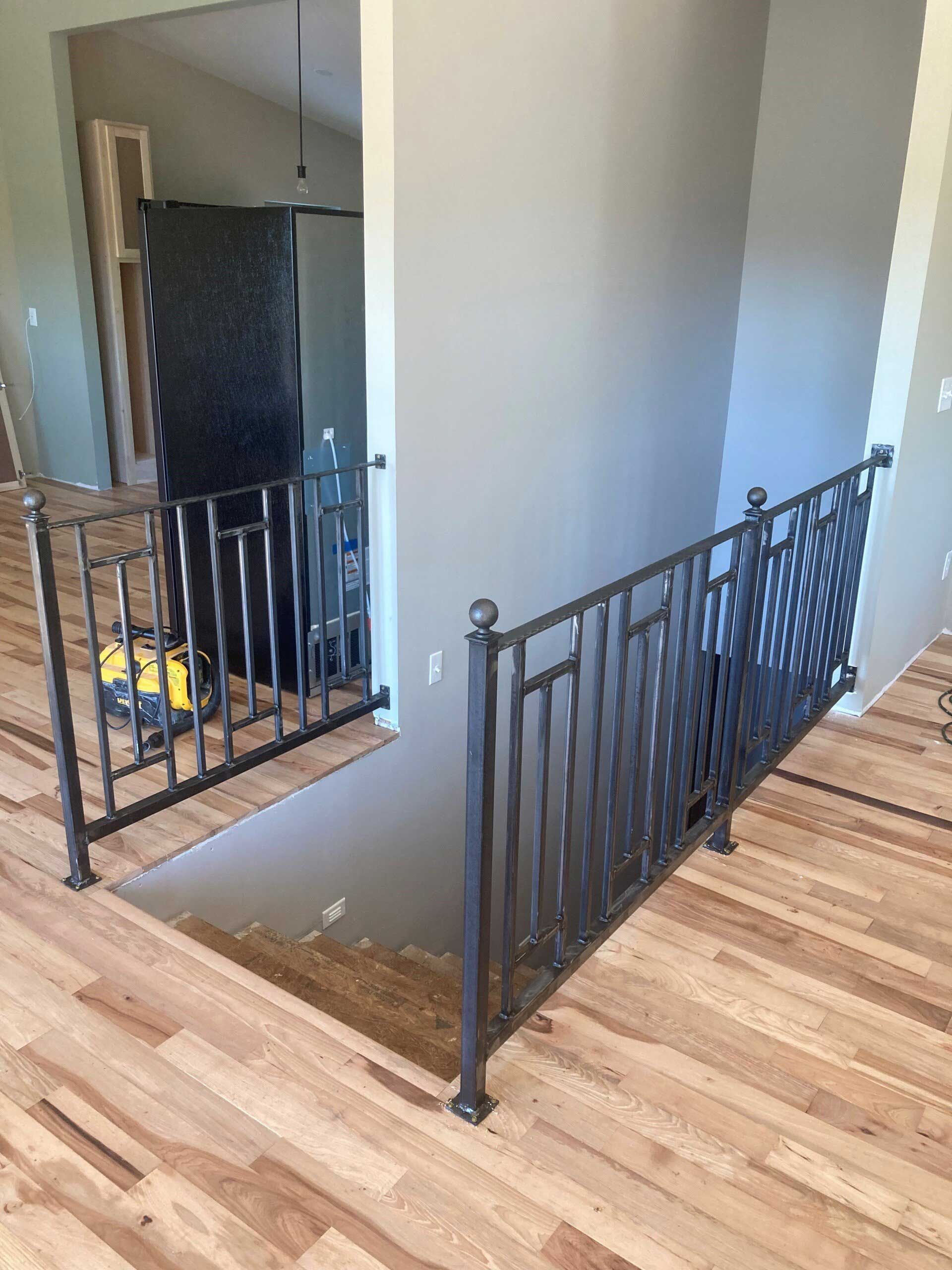Staircase with metal railing. Light wood flooring, gray walls. Refrigerator visible in the background.