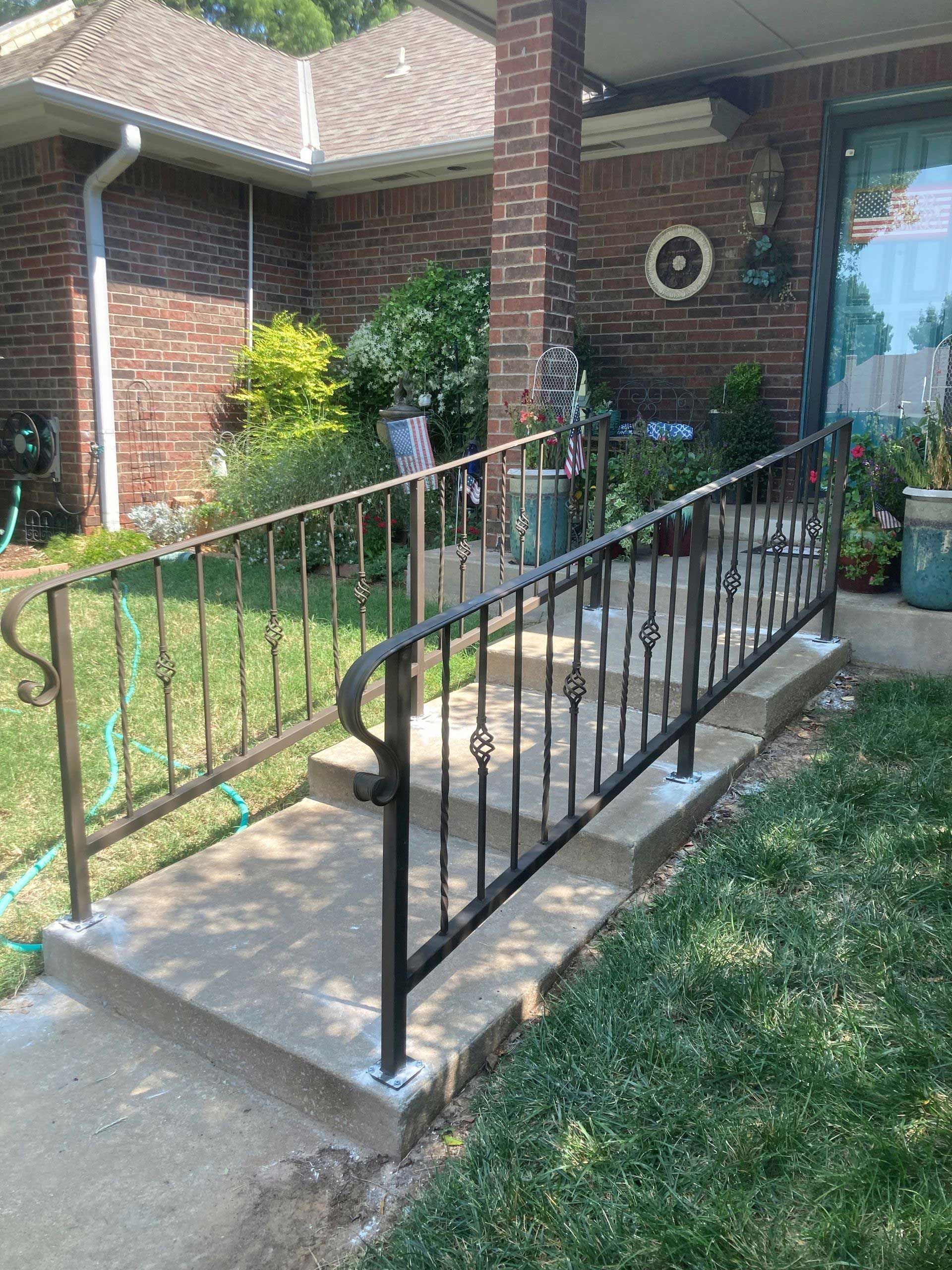 Concrete ramp with black metal railings leading to a brick home's porch. Green grass surrounds.
