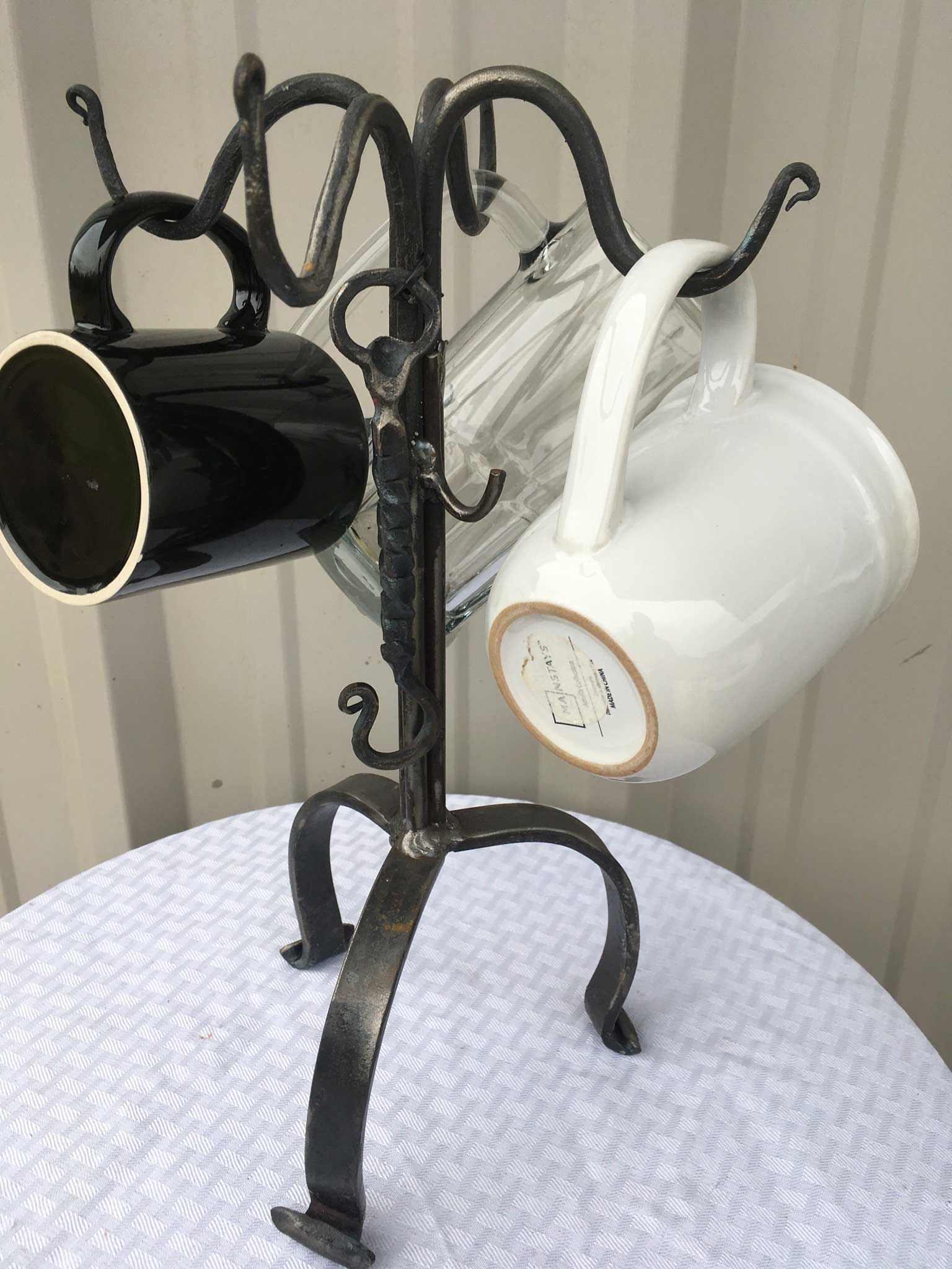 Black wrought iron mug holder with three mugs, on a white table.