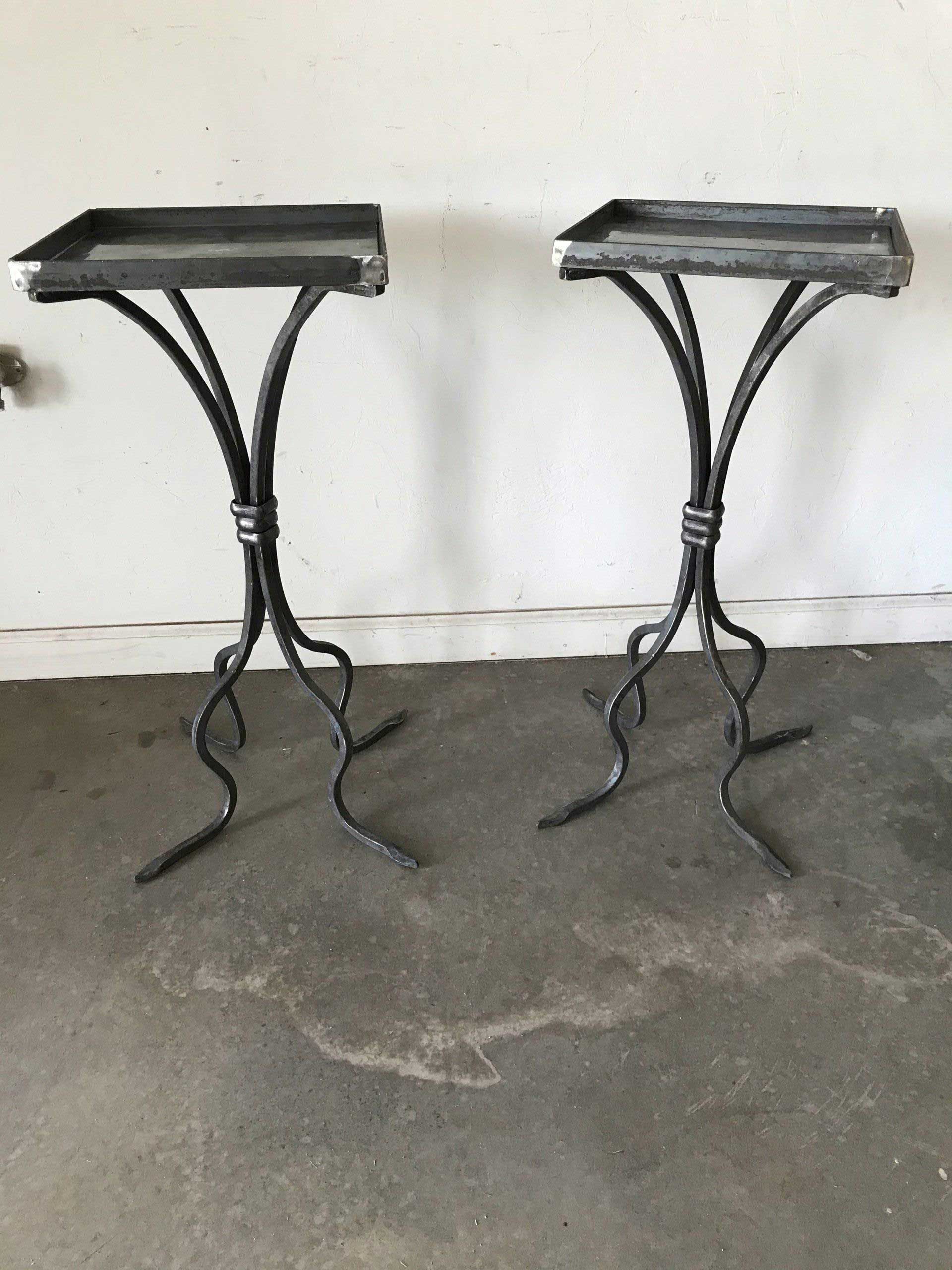 Two ornate, black metal side tables on a concrete floor, against a white wall.