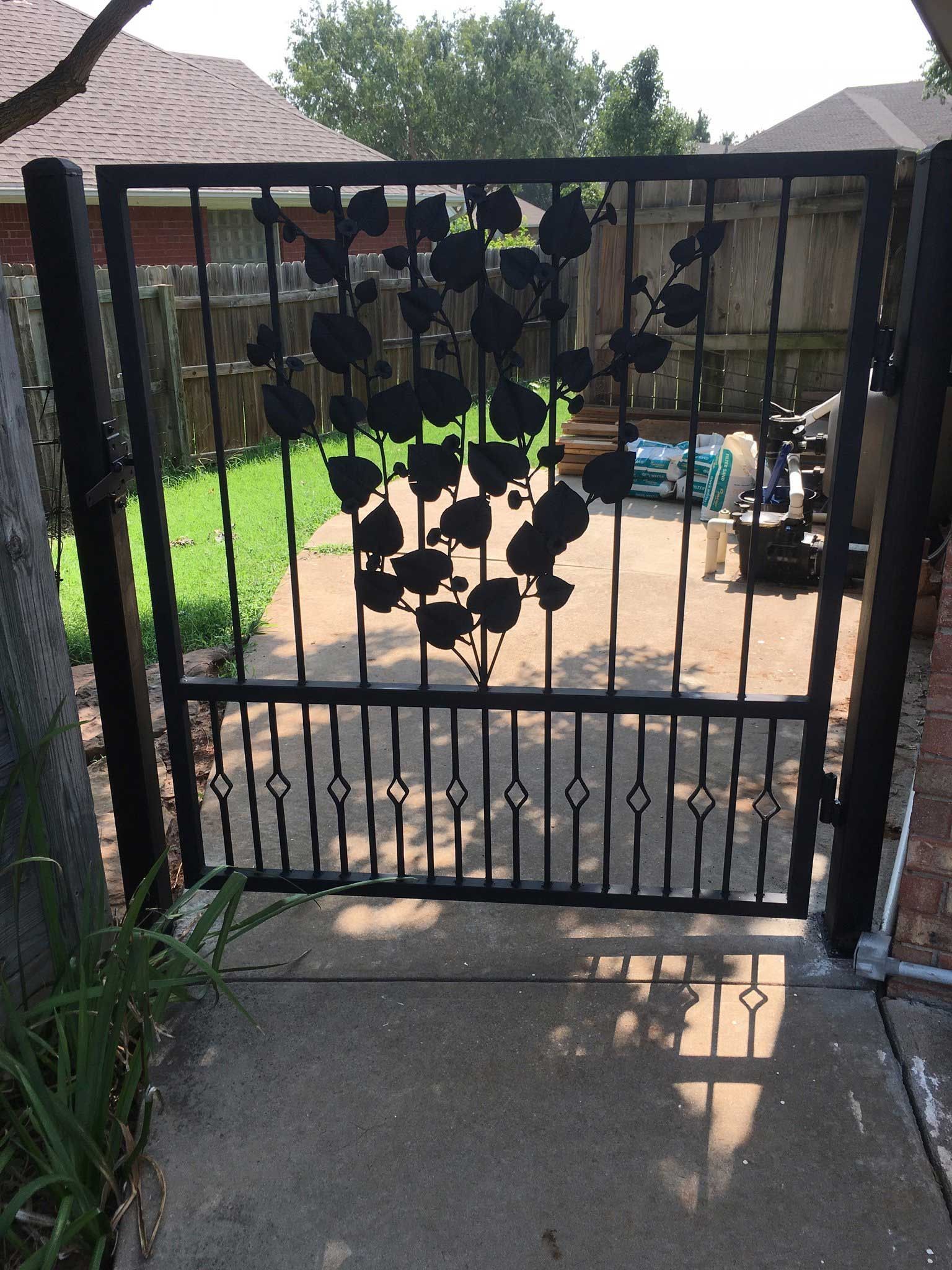Black metal gate with floral design, set in concrete, leading into a yard.