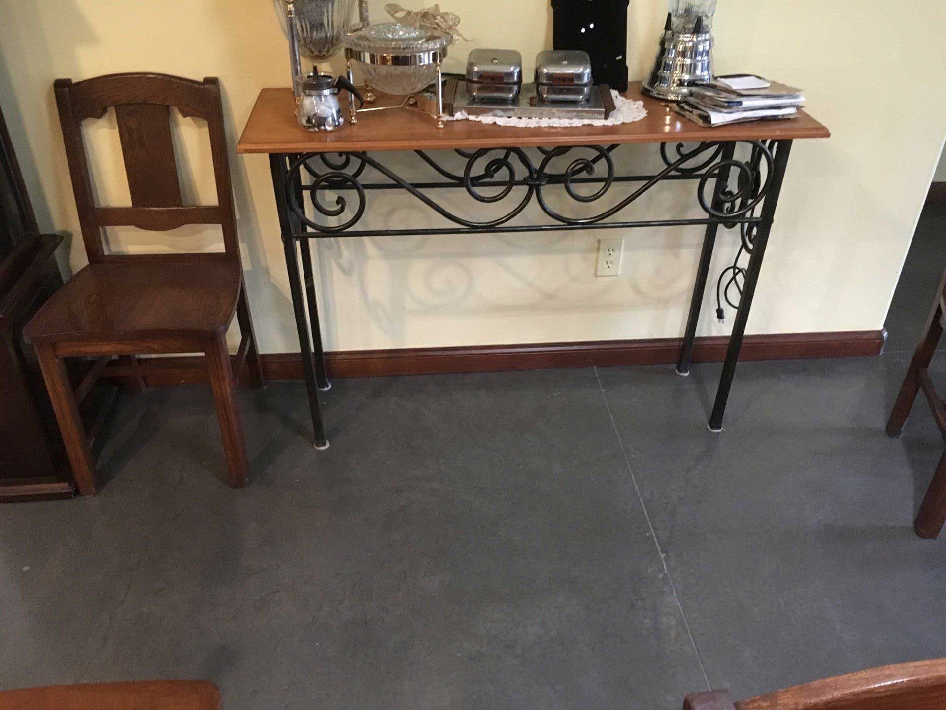 A console table with a wooden top and wrought iron base holds serving dishes. A chair sits to the left.