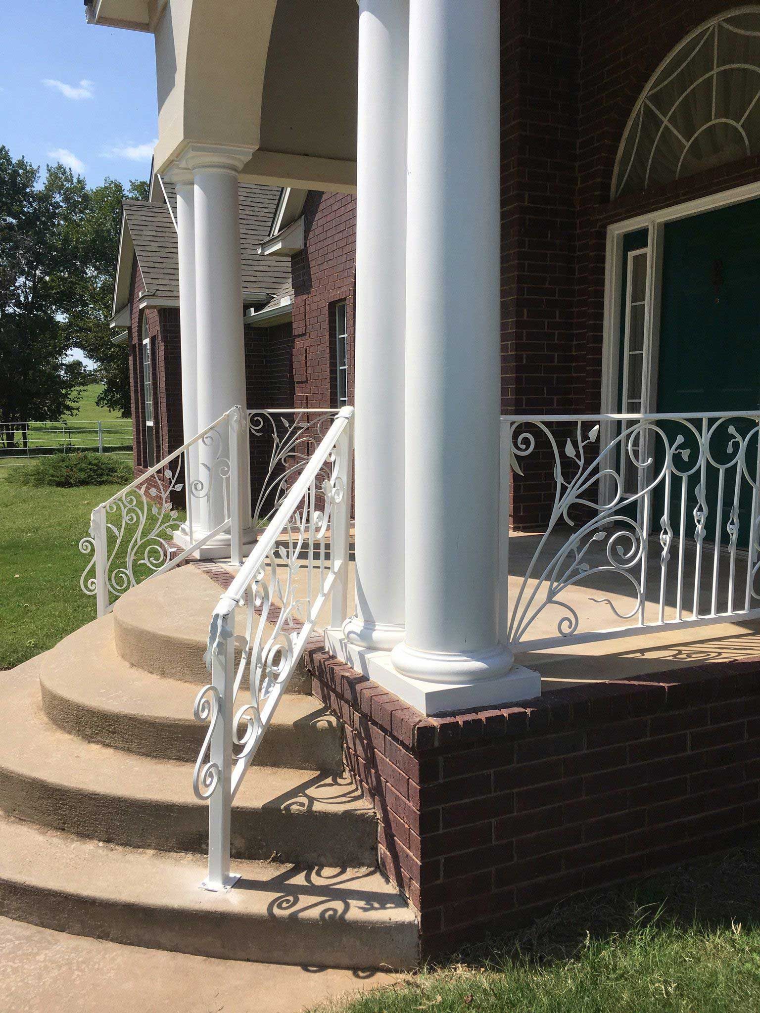 White pillars and ornate railing on a brick building's porch with steps.