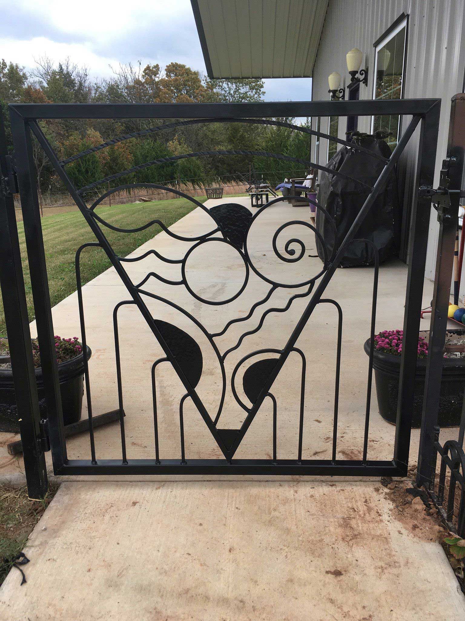 Black metal gate with geometric design, on a concrete patio.