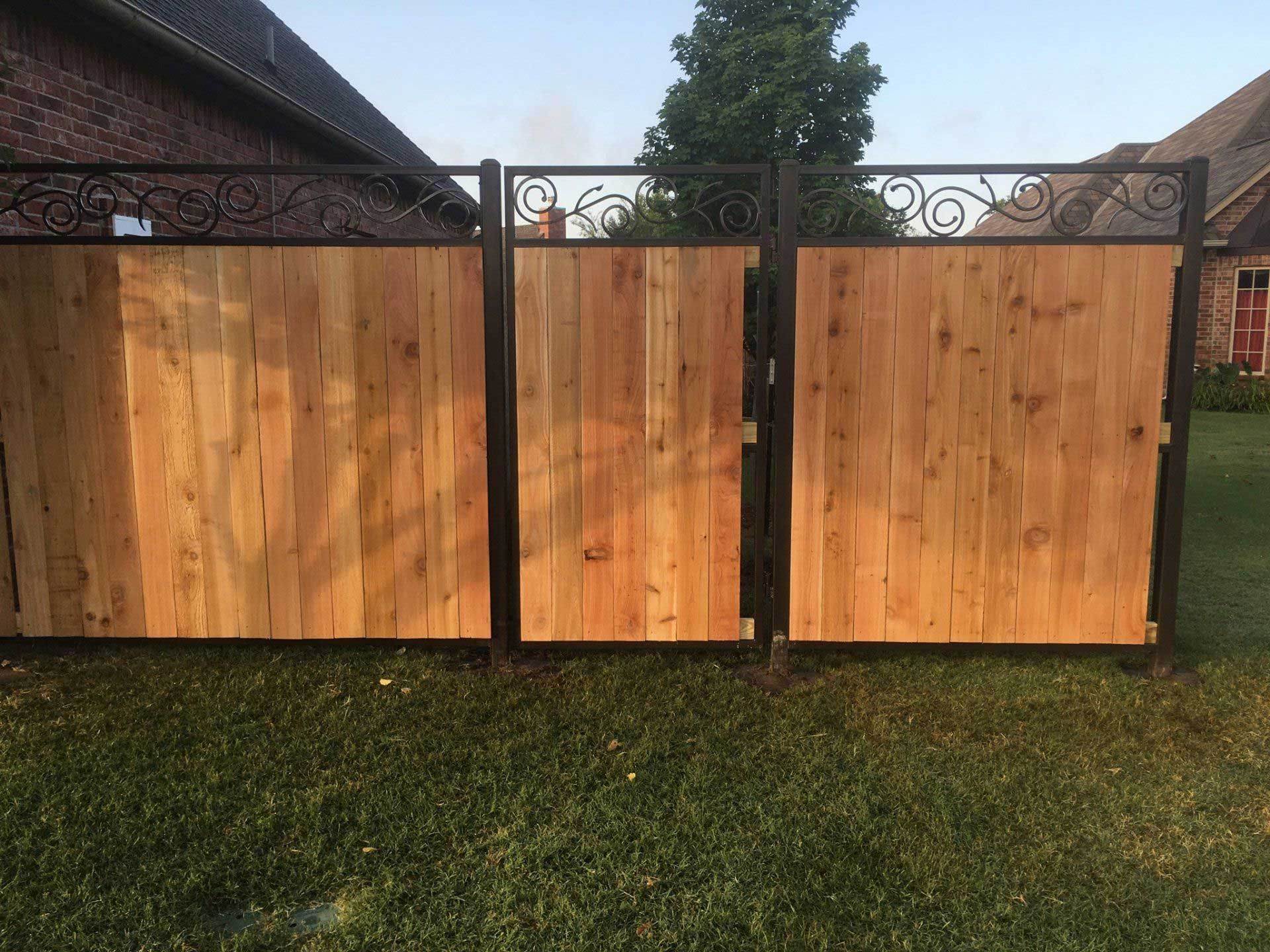 Wooden fence with decorative wrought iron top panels and gate in a grassy yard.