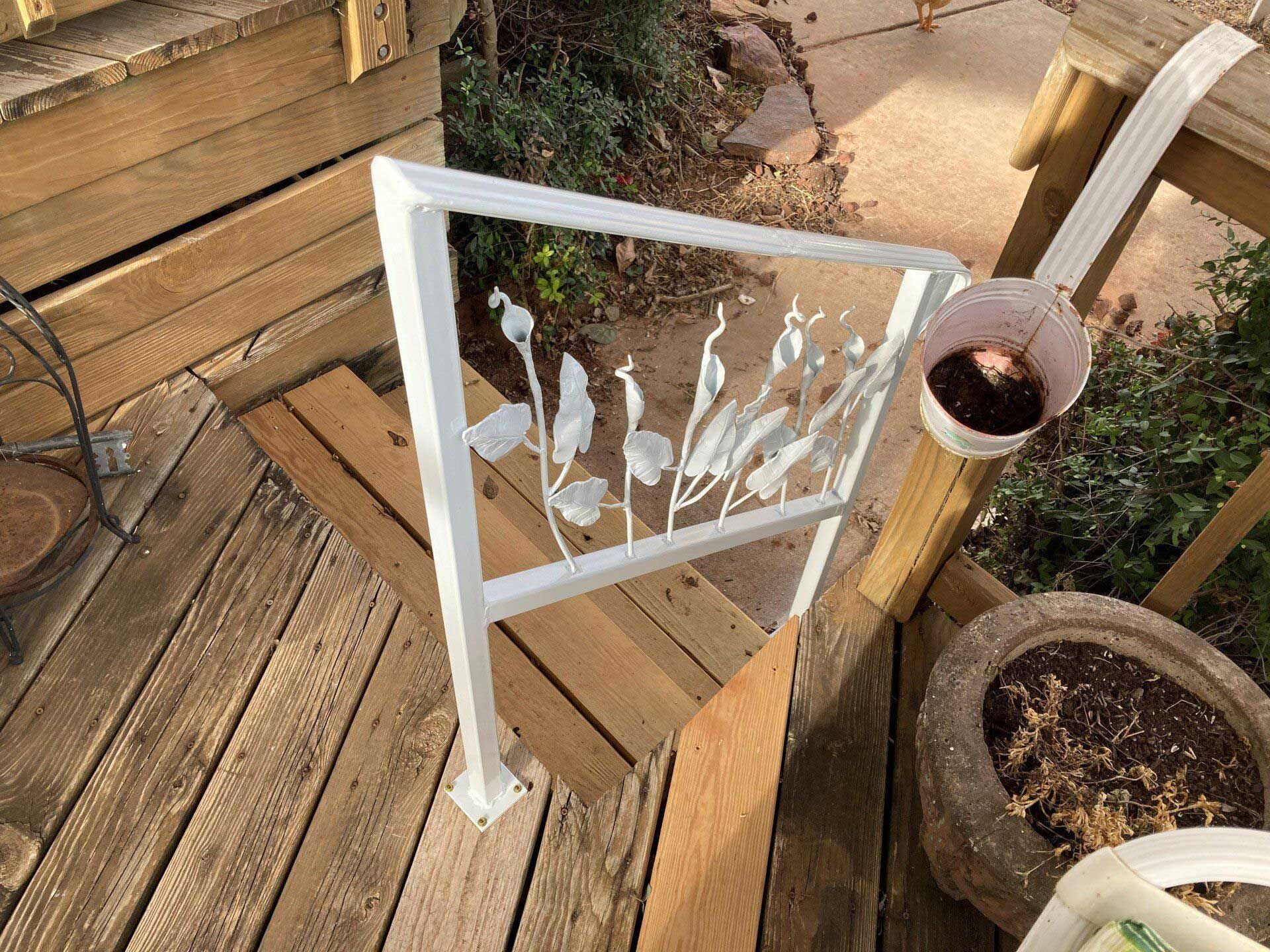 White metal railing with floral design on wooden steps, potted plants.