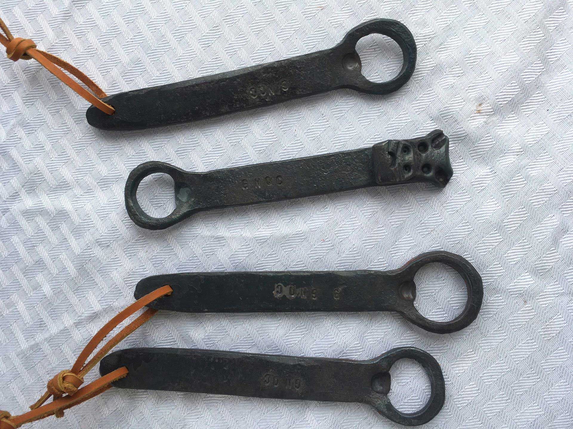 Four small, dark metal tools with key rings, three with leather cords attached.