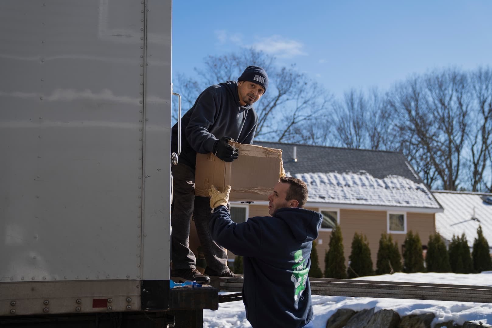 Two men unloading a box from a truck on a snowy day.