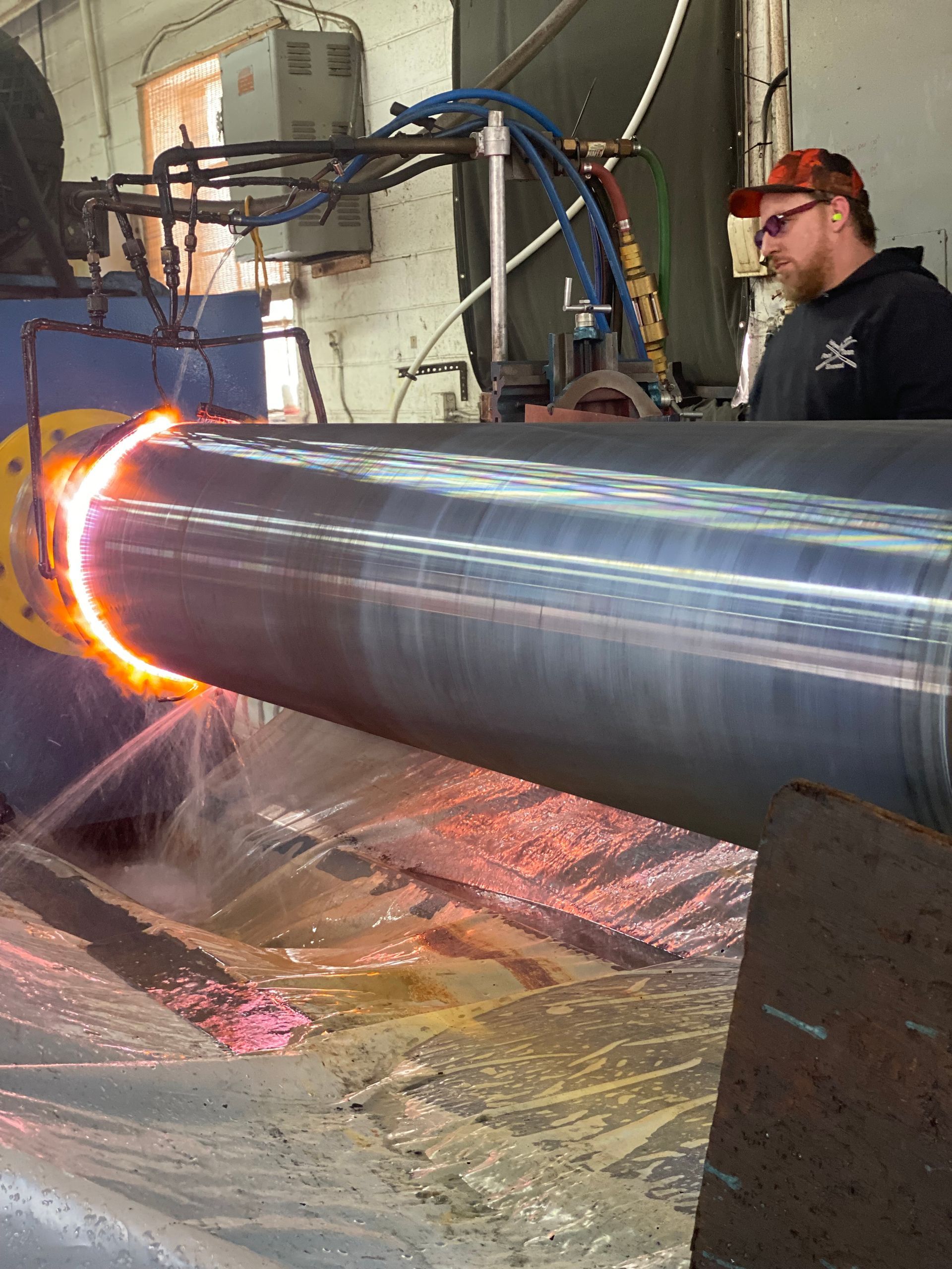A worker uses a heat treatment process on a large metal cylinder. Sparks and water are present.