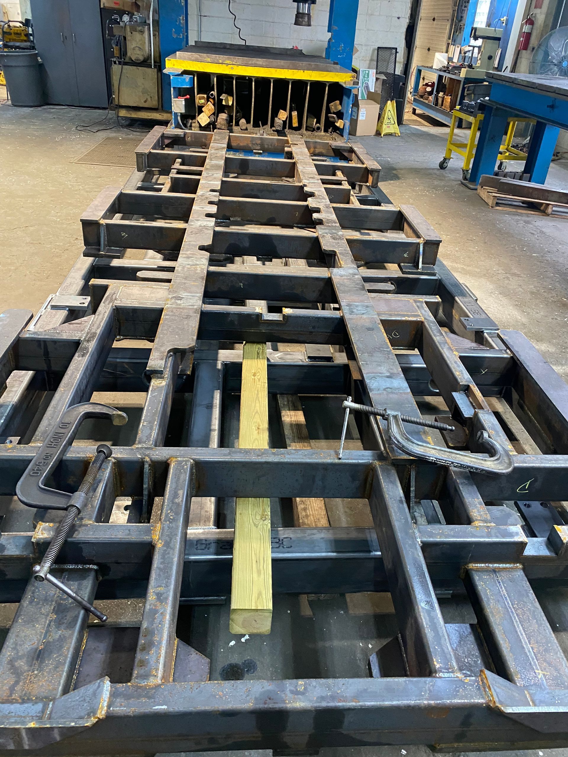 Metal framework with wooden beams, clamps, and a machine press in a factory.