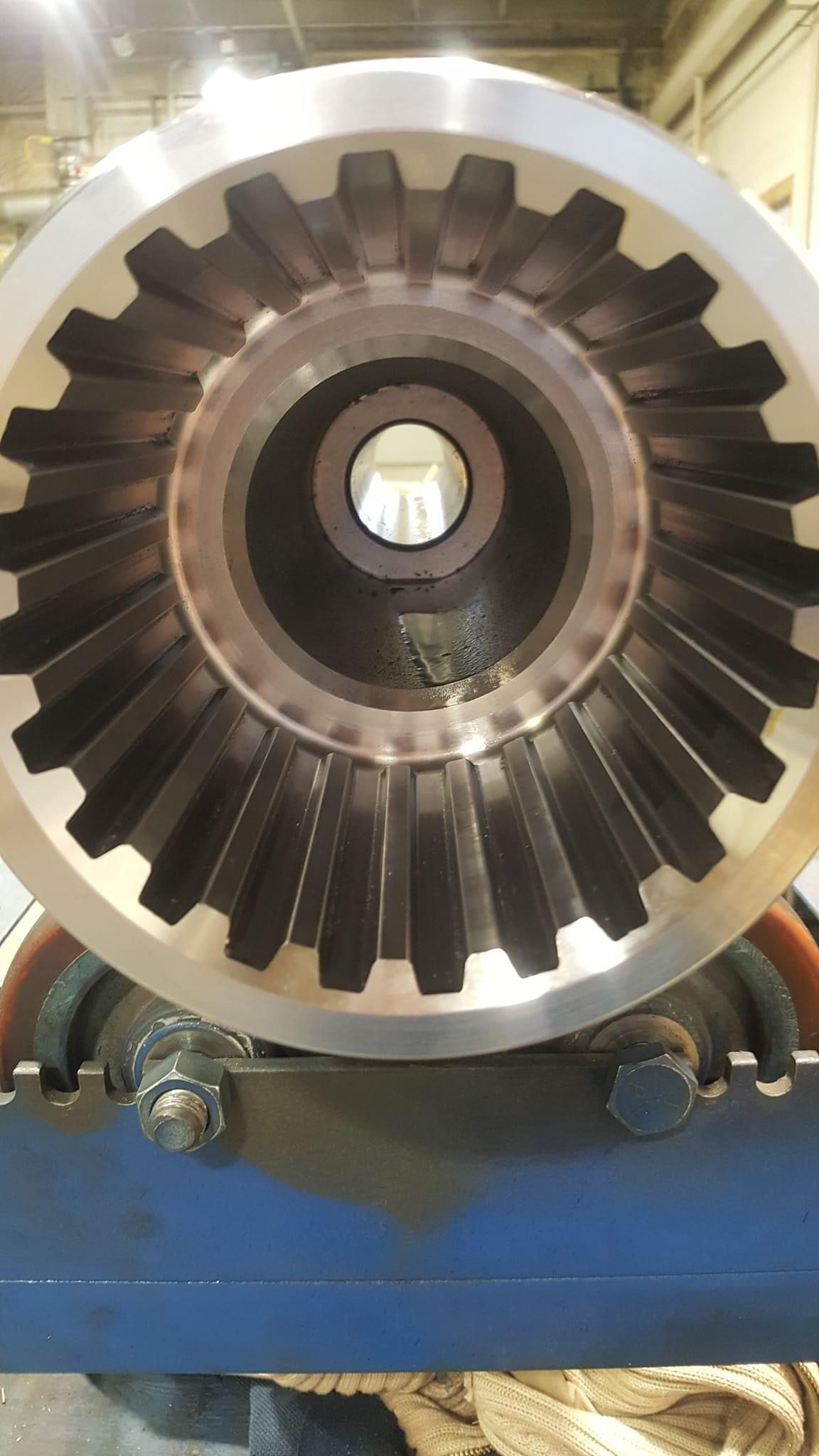 Cross-section of a large, toothed metal gear, viewed from the open end, mounted on a blue support.