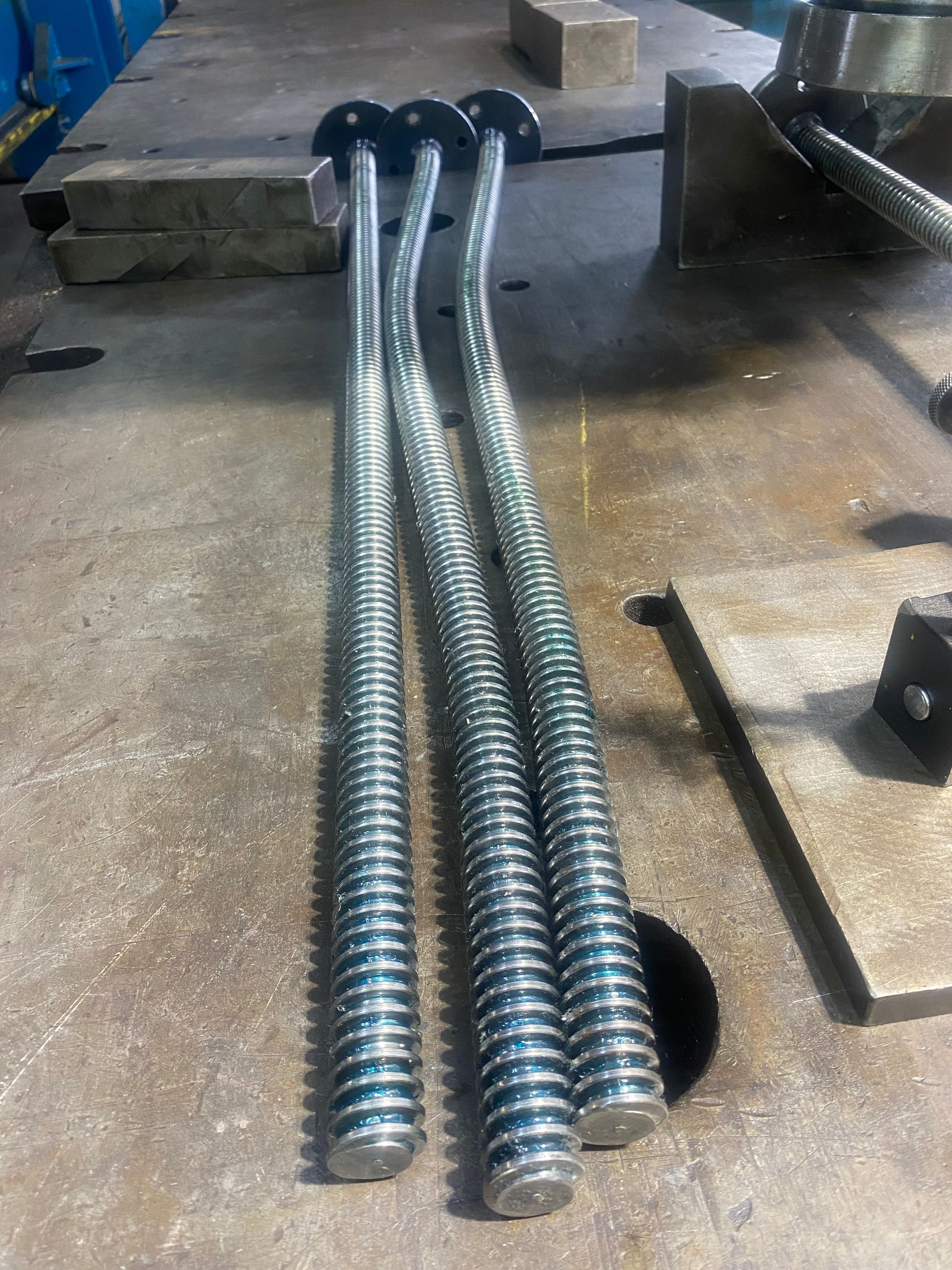 Three curved, threaded metal rods with circular heads resting on a metal surface.